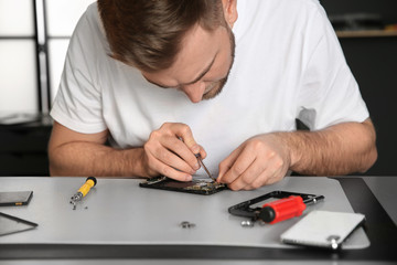 Naklejka premium Technician repairing mobile phone at table in workshop