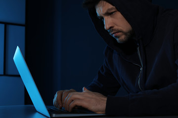 Man using laptop in dark room. Criminal offence
