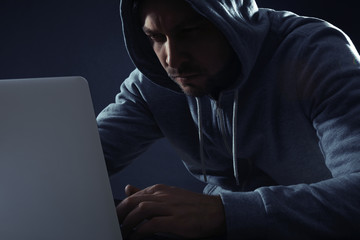 Man using laptop on dark background. Criminal activity