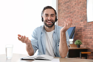 Young man with headset looking at camera and using video chat in home office