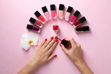 Woman applying bright nail polish on color background, top view