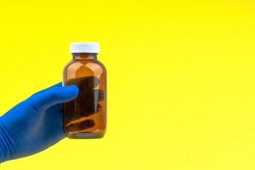 Hand in a blue glove holding bottle on yellow background