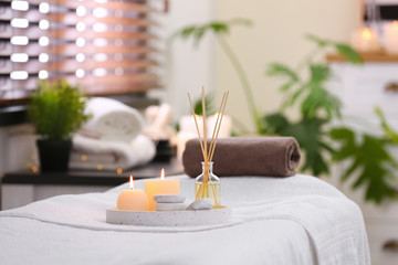 Composition with reed air freshener, candles and stones on massage table in spa salon