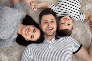 Happy parents and their son lying together on floor, view from above. Family time