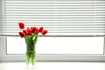 Bouquet of beautiful tulips in vase near window with blinds. Space for text