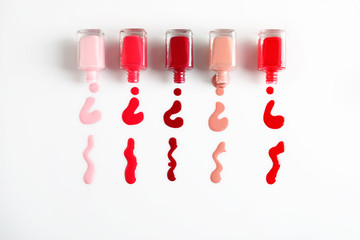 Spilled colorful nail polishes and bottles on white background, top view