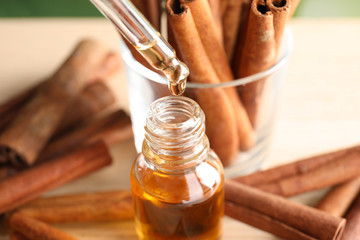 Pipette with essential oil over bottle and cinnamon sticks on table, closeup