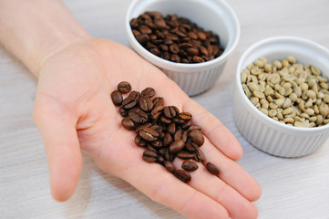 Roasted and green unroasted coffee in bowls. Freshly roasted coffee beans on the palm closeup