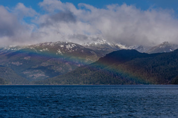 Scene view of a colorful rainbow over a lake against Andes mountains, Los Alerces National Park, Argentina