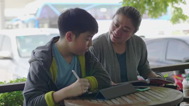 Asian boy is playing tablet computer and talking with his mother , smile face.