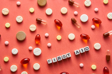 Black and white title FIRST AID from white cubes on the table with tablets on coral background
