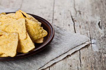 Mexican nachos chips on brown ceramic plate on linen tablecloth.