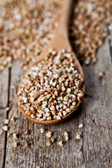 Organic green dry buckwheat seads in wooden spoon closeup on rustic  background.