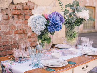 The decor and table setting for a meal or a holiday. Tablewares on a table against a brick wall. A bouquet of colorful flowers. Tableware and decor