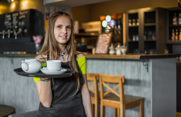 Portrait young waitress standing in cafe.  girl the waiter holds in bunches a tray with utensils....