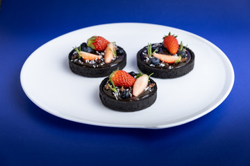Cookie crust chocolate tart with Blueberry and strawberry set on Blue Background.