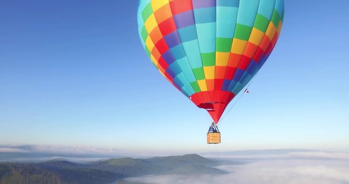 Colorful hot air balloon epic flying above mountain over the fog at sunrise with beautiful sky background - Aerial drone view