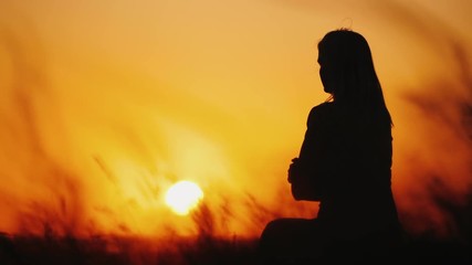 Silhouette of a woman in high grass at sunset. Grass swaying in the wind