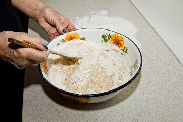 female hand kneads dough from milk of butter and flour in a metal bowl with a wooden whisk in the kitchen