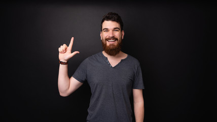 Fototapeta premium Photo of a bearded man pointing up and loooking at camera over dark background