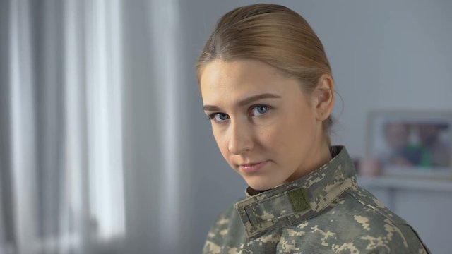 Confident female soldier student looking at camera, standing near academy window