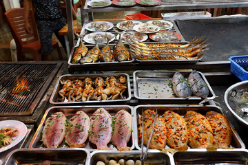 Traditional asian night market with delicious seafood and exotic food for tourist. Marinated fish and frogs on the counter of a street restaurant for grilling. Night photo under fluorescent light