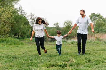 Fototapeta premium Happy family: mother father and child son on nature on sunset. Mom, Dad and kid laughing and hugging, enjoying nature outside. Sunny day, good mood. concept of a happy family