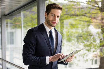 Gesch&auml;ftsmann mit Tablet steht am Fenster und schaut selbstbewusst 