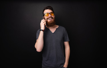 Photo of cheerful bearded guy talking on smartphone over dark isolated background