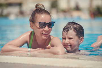 The portrait of smiling mom and son in the swimming pool of luxurious hotel, they are having fun during summer vacations.