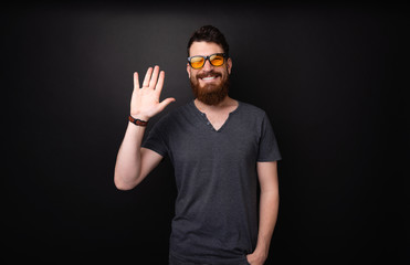 Obraz premium HI DUDE! Photo of handsome bearded guy doing saluting gesture over dark background