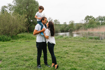 Fototapeta premium Happy family: mother father and child son on nature on sunset. Mom, Dad and kid laughing and hugging, enjoying nature outside. Sunny day, good mood. concept of a happy family