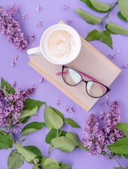 Fototapeta na wymiar Cappuccino, book with glasses, violet lilac flowers, morning concept