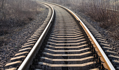 Obraz premium Wide railroad track with concrete sleepers (cross ties), turning left, close-up, backlight, selective focus