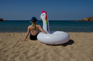 Woman relaxing on beach with inflatable unicorn pool tube on beach near sea