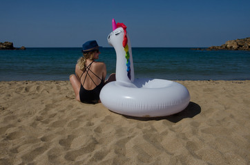 Woman sitting with inflatable unicorn pool float on beach sand near sea