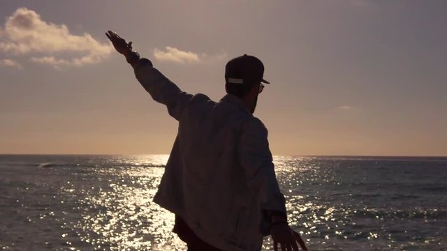 Silhouette di un ragazzo che fa l'aeroplano con le braccia al tramonto di fronte all'Oceano. Concetto di Libert&agrave; 