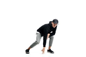Young man wearing a black sweatshirt, gray pants, cap and sneakers dancing street dances on a white background