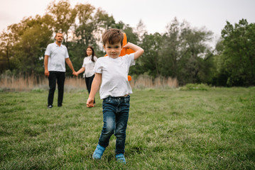 Obraz premium Father, mother and son playing with toy airplane in the park. friendly family. People having fun outdoors. Picture made on the background of the park and blue sky. concept of a happy family.