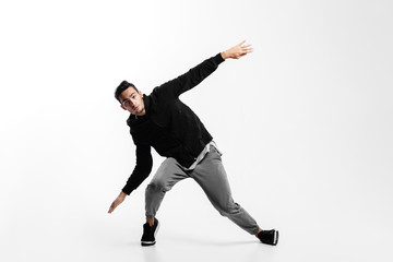 Stylish young man is dancing hip-poh on a white background. He is bending his knees and spreading his arms to the sides