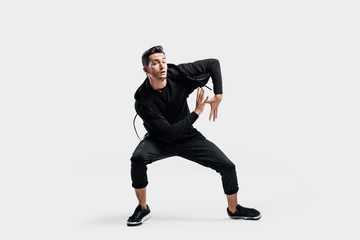 Dark-haired young  man dressed in a black clothes is dancing street dance. He makes stylized movements with his hands