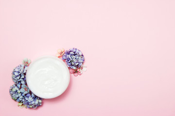 A jar of cream with flowers on a pink background. Top view.