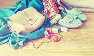 Female handbag, shawl, nail polish and shoes on a wooden background, toned.