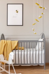 Grey crib, bee decoration and graphic, and rocking horse in a kid room interior