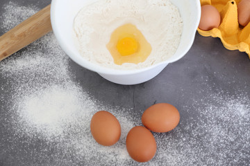 Preparation of the dough. Flour, eggs and a kitchen towel. A bunch of flour on a wooden spoon, a broken egg in a bowl of flour, egg shell and lots of eggs on the plate. Baking, top view.