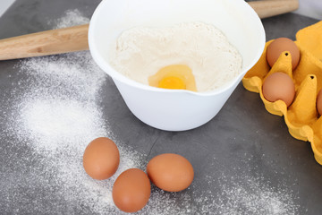 Preparation of the dough. Flour, eggs and a kitchen towel. A bunch of flour on a wooden spoon, a broken egg in a bowl of flour, egg shell and lots of eggs on the plate. Baking, top view.