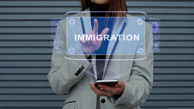Unrecognizable business woman, interacts with a HUD hologram with text Immigration. Girl in a business suit uses the technology of the future mobile screen against the background of a striped wall