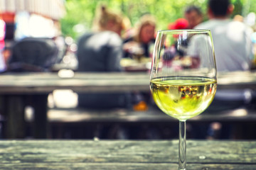 Sipping a white wine glass outside on a bench with people blurred in background