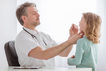 Obraz premium Sick little boy with flu and pediatrician checking his sore throat