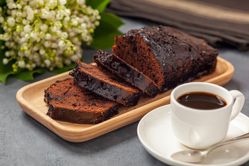 Ciasto czekoladowe na drewnianej tacce, kawa, konwalie i ścierka kuchenna